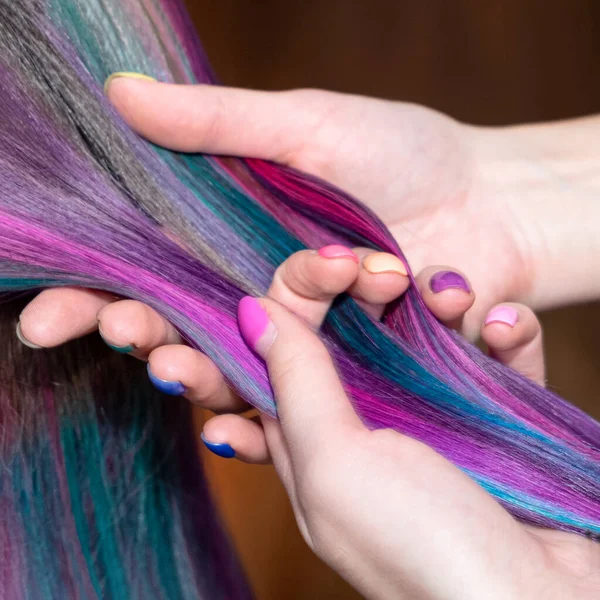 girl with beautiful nails, beautiful manicure combs her daughter with creative colored hair.