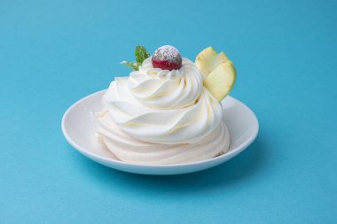 Pavlova kremalı tatlı, beyaz tabakta, mavi arka planda. Kremalı, yuvarlak kremalı kremalı krema, nane yapraklı ve kirazlı tatlı.