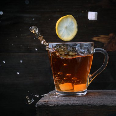 Bir dilim limon ve bir küp şeker, bir bardak koyu siyah çayın içine düşer. Donmuş su damlaları koyu bir ahşap zemine düşer..