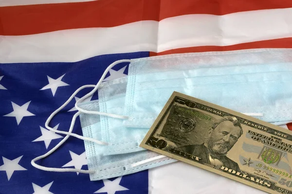 paper American money, a banknote on medical masks against an American flag. The concept of material assistance and protection of the American people from pandemic.