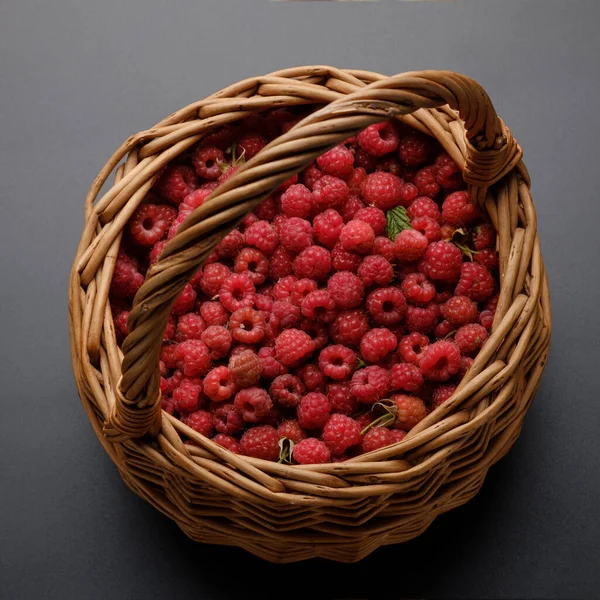 wicker basket with red sweet raspberries on a dark, gray-black background