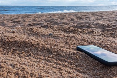 Gri kumlara gömülü cep telefonu, tatildeyken kumsalda akıllı telefonunu kaybetmek..