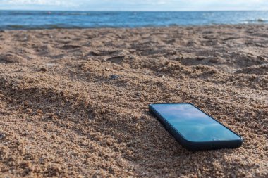 Gri kumlara gömülü cep telefonu, tatildeyken kumsalda akıllı telefonunu kaybetmek..