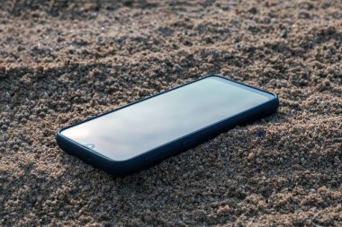 Gri kumlara gömülü cep telefonu, tatildeyken kumsalda akıllı telefonunu kaybetmek..