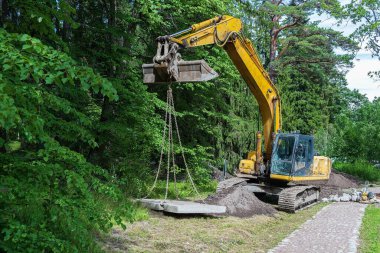 Seçici odaklanma, parktaki bir kazıcı beton döşemeler. Kanalizasyon hattını aşıyorum. Kargo yüklemek, taşımak ve taşımak için inşaat malzemeleri. Kazı makinesi toprak işlerinde bir inşaat alanında çalışıyor..