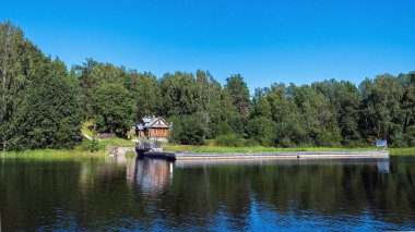 Panoramik fotoğraf, ahşap bir münzevi evi evi ve mavi suyu olan güzel bir gölün kıyısında büyük bir ahşap iskele.