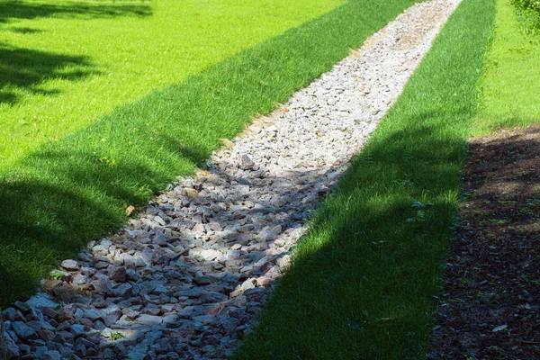 seçici odak, drenaj, bir park bölgesinde drenaj sistemi, çimlerle kaplanmış ve taşlarla kaplanmış bir su yolu, doğa ve yol arasında bir su kemeri. Çim tarlasında taştan su çekiliyor. Çim ve bitki koruması.