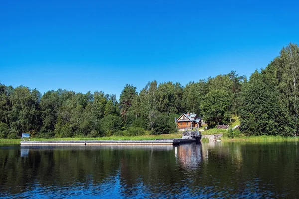 Bitkilerle çevrili bir adada büyük bir ahşap iskelesi olan eski bir İskandinav evi İskandinavya 'da kayalık bir sahilde duruyor.