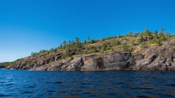 Güneşli bir günde sudan çıkan mavi sular ve ağaçlarla kaplı kayalar, Ladoga Gölü 'ndeki Valaam Takımadaları' nın güzel adaları, Rusya, Karelia.