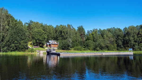 Panoramik fotoğraf, ahşap bir münzevi evi evi ve mavi suyu olan güzel bir gölün kıyısında büyük bir ahşap iskele.