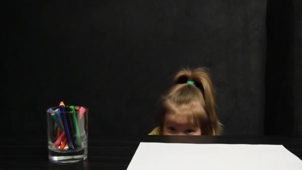 Ragazzina nascosta sotto il tavolo mentre disegna. Forse ha paura di qualcosa. . — Video Stock