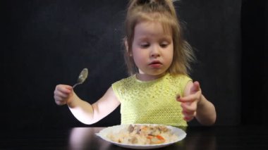 Çocuk siyah masada siyah bir arka plan üzerinde bir kaşık ile pişmiş pirinç ve mantar yiyor