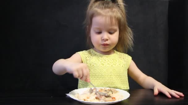 3 year old child eats cooked rice and mushrooms with a spoon on a black background at the black table — Stock Video
