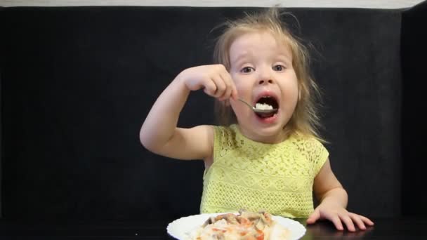 3歳の子供は黒いテーブルで黒い背景にスプーンで炊いた米とキノコを食べる — ストック動画