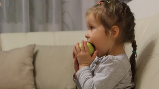 La mano femenina le da una manzana a un niño. El niño comiendo manzana verde viendo la televisión — Vídeos de Stock