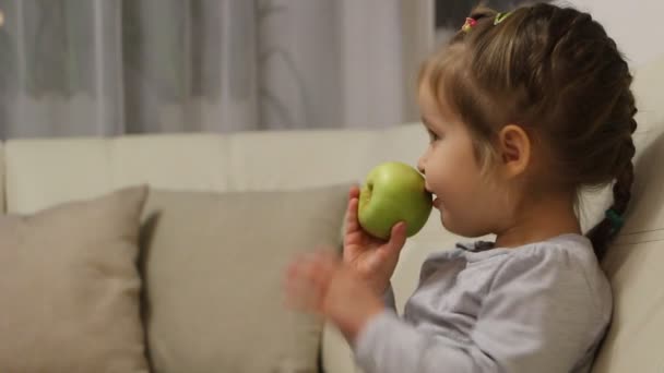 Klein meisje eet groene appel tijdens het kijken naar TV — Stockvideo