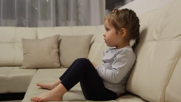 Petite fille assise sur le canapé et regardant la télévision — Video