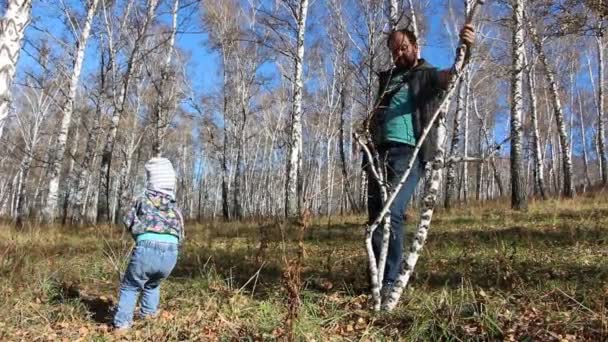 Батько і дочка створюють арт-об'єкт з гілок сухого дерева в осінньому лісі . — стокове відео