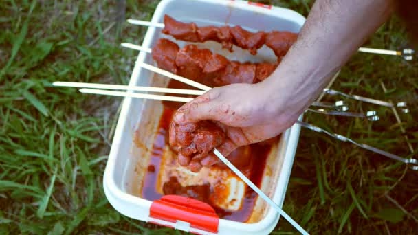 Um homem empurrou pedaços de carne crua com um espeto. Cozinhar kebab ao ar livre — Vídeo de Stock