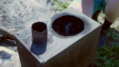 Bir adam, paslı bir açık hava sobasında kağıt kullanarak ateş yakıyor..