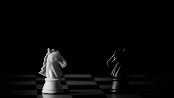 Siyah arka planda satranç tahtasında beyaz ve siyah at karşılaşması. - İş lideri ve dövüş konsepti.