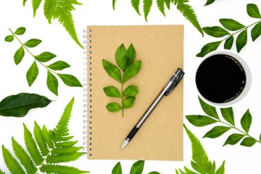 Beyaz arkaplanda yeşil yapraklı bir kitap üzerindeki bir kalem.