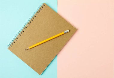 Kahverengi defter ve mavi ve pembe arka planda sarı kalem.