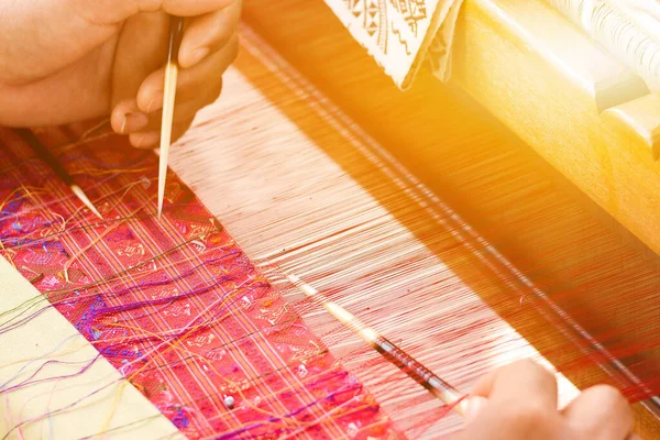 hand of a women works on silk weaving with traditional hand weaving loom.