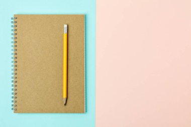 Kahverengi defter ve mavi ve pembe arka planda sarı kalem.