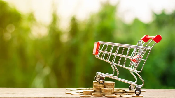 Alışveriş arabası ve ahşap masada bir yığın altın para. - Reklam ve fotokopi alanı için..