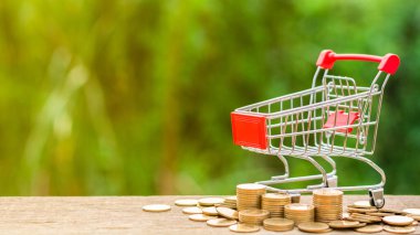 Boş alışveriş arabası ve ahşap masada bir yığın altın para. - Reklam ve fotokopi alanı için..