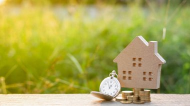 Küçük ev modeli ve altın sikke yığınlı bir saat. - gelecek planlama konsepti için yatırım ve tasarruf.