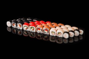 Suşi Roll - Somon balığı, füme yılan balığı, salatalık, krem peynir, susam, Avokado, soğan kızartması, yengeç eti, siyah zemin üzerinde izole edilmiş Tobiko ile Maki suşi parçaları koleksiyonu
