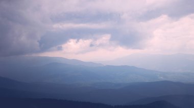 Karpat Dağları. Yaz dağlarındaki yeşil tepelerin manzarası. Mavi gökyüzünün altındaki puslu yeşil dağ ormanı.