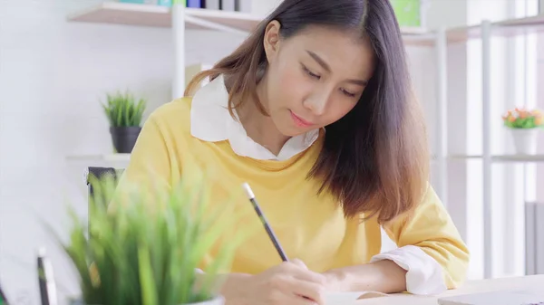 Asian woman learning and writing in book on table at home