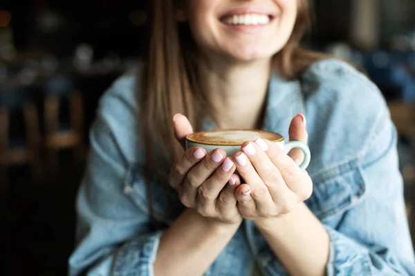 Молодая девушка улыбается и пьет вкусный кофе — стоковое фото