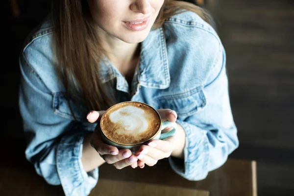 Молодая девушка улыбается и пьет вкусный кофе — стоковое фото