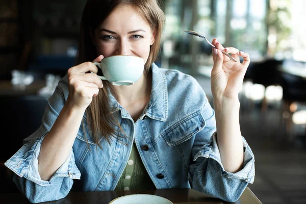 Молодая женщина пьет кофе улыбаясь и подмигивая — стоковое фото
