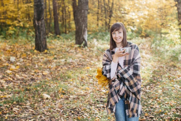 Девушка в осеннем лесу пьет чай с листьями в руках. Девочка в отличном настроении и счастлива — стоковое фото