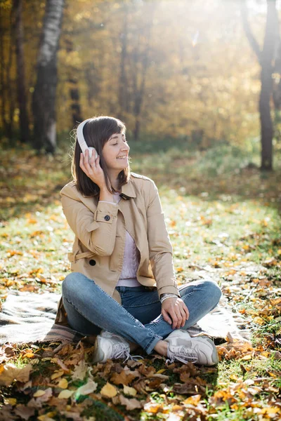 Молодая девушка слушает музыку в наушниках в осеннем лесу. Девочка в отличном настроении и счастлива — стоковое фото