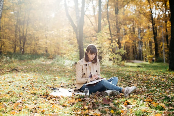 Une jeune fille dessinant près d'un lac dans la forêt d'automne. J'esquisse. La fille est de bonne humeur et heureuse — Photo