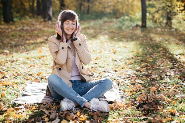 Niña escuchando música con auriculares en el bosque de otoño. La chica está de buen humor y feliz. —  Fotos de Stock