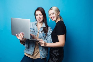 Spor kıyafetleri giymiş iki mutlu ve neşeli kız, en iyi arkadaşlar eğleniyor ve dizüstü bilgisayardan fotoğraf izliyorlar.