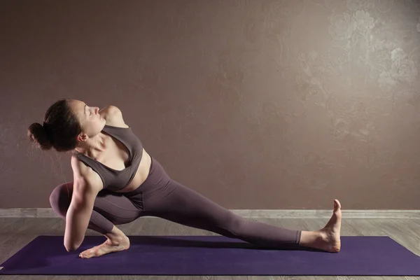 Joven mujer atractiva deportista practicando yoga, meditando en pose de yoga, haciendo ejercicio, usando ropa deportiva, estudio de yoga marrón — Foto de Stock