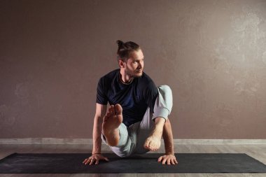 Genç sporcu yoga yapıyor, yarım Lotus pozisyonunda meditasyon yapıyor spor kıyafetleri giyiyor, kapalı alanda yoga yapıyor, kahverengi yoga stüdyosu.