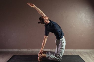 Genç sporcu yoga yapıyor, Yarım Lotus pozisyonunda meditasyon yapıyor spor kıyafetleri giyiyor, kapalı alanda uzun, gri yoga stüdyosu.