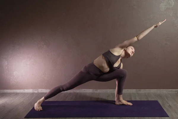 Joven mujer atractiva deportista practicando yoga, meditando en pose de yoga, haciendo ejercicio, usando ropa deportiva, estudio de yoga marrón — Foto de Stock