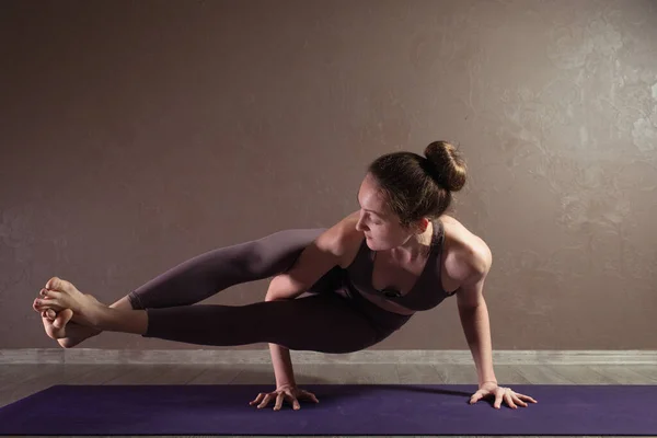 Joven mujer atractiva deportista practicando yoga, meditando en pose de yoga, haciendo ejercicio, usando ropa deportiva, estudio de yoga marrón —  Fotos de Stock