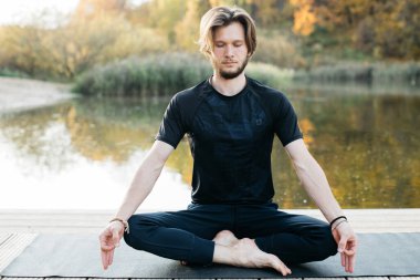 Genç adam göl manzaralı doğada yoga yapıyor. Akşam sporu, spor ve sağlıklı yaşam tarzı.