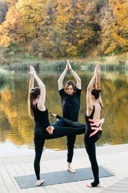 Genç kadınlar ve erkek göl manzaralı doğada yoga yapıyorlar. Akşam sporu, spor ve sağlıklı yaşam tarzı.